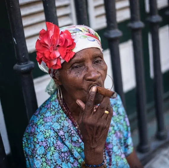 Femme cubaine vetue de bleue avec une fleur sur la tete fumant le cigare