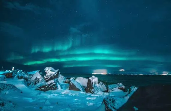 Roches enneigées en bord de mer sur fond d'aurores boréales en Islande