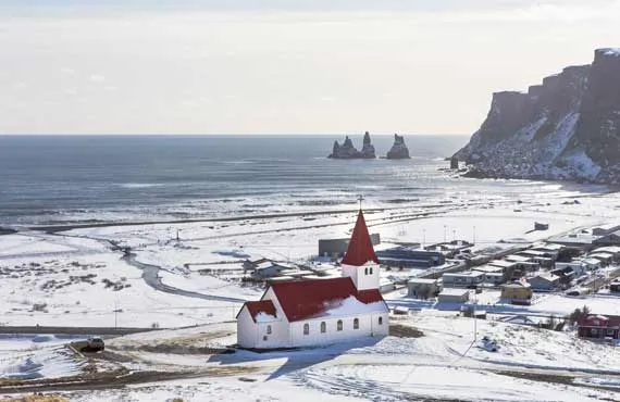 Petite église blanche au toit rouge dans un village en bord de mer dans un paysage enneigé