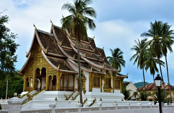 Temple au toit pointu et à la façade dorée entouré de palmiers